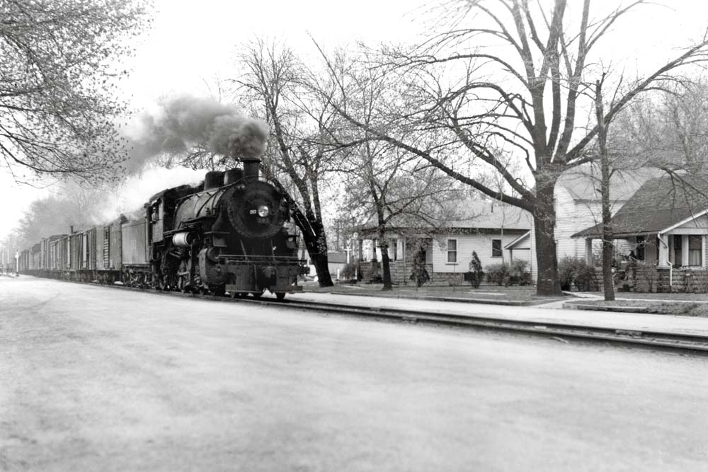 Steam locomotive pulls freight train down street trackage from Monon Railroad history