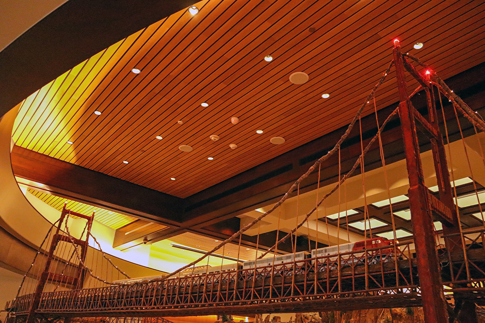 A streamlined train crosses a massive suspension bridge