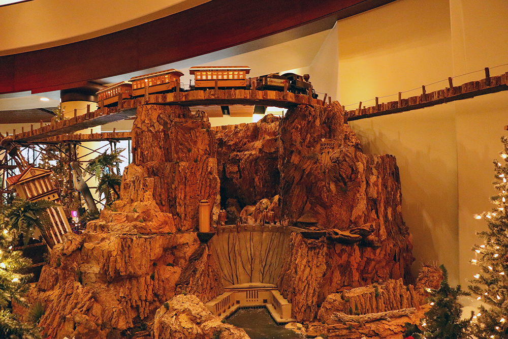 A steam train crosses a bridge over a model of the Hoover Dam