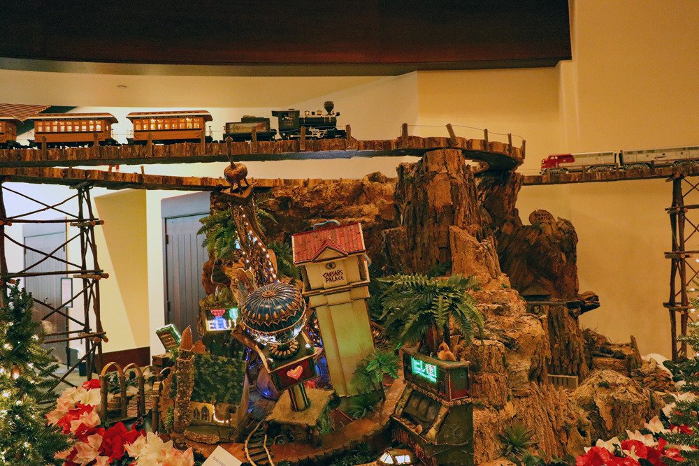 A steam train meets a diesel train on a bridge above a model of Las Vegas