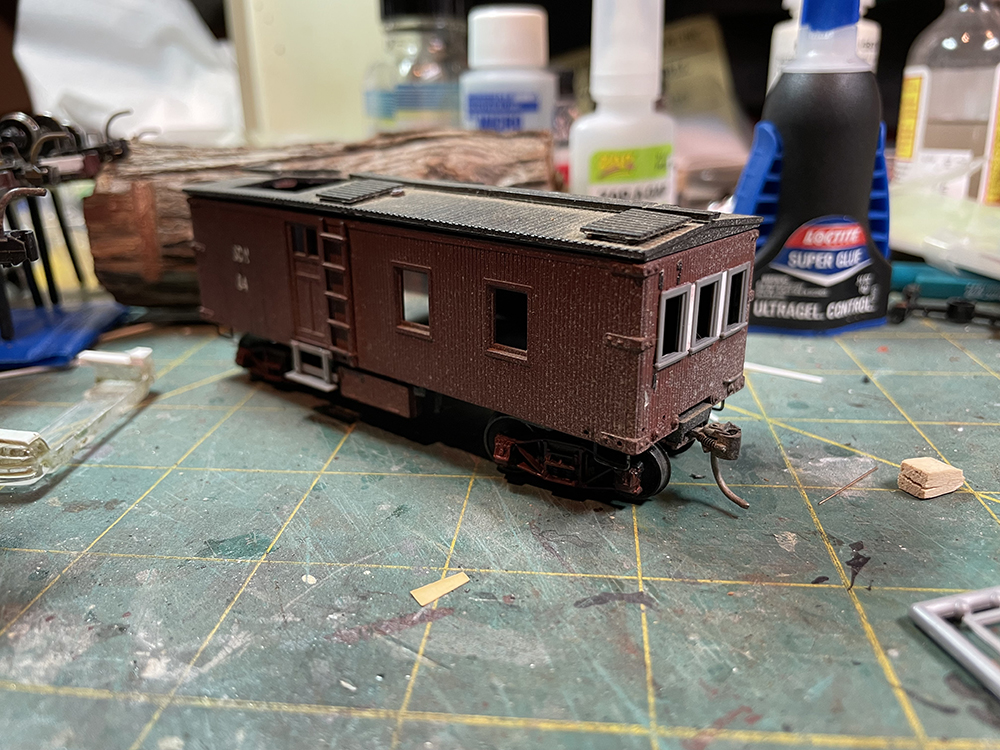 Brown model wood-sided caboose sitting on red trucks and wheels with gray windows