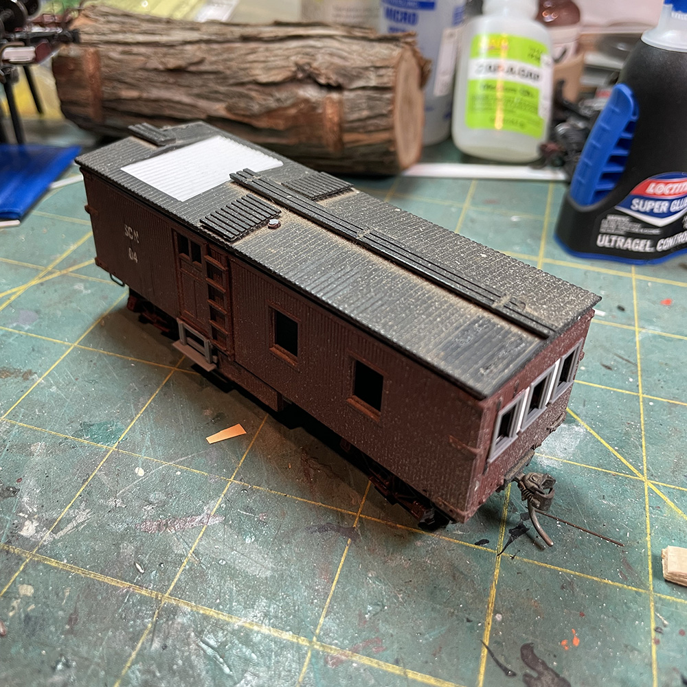 Brown model wood-sided caboose viewed from top with white panel filling large hole in roof