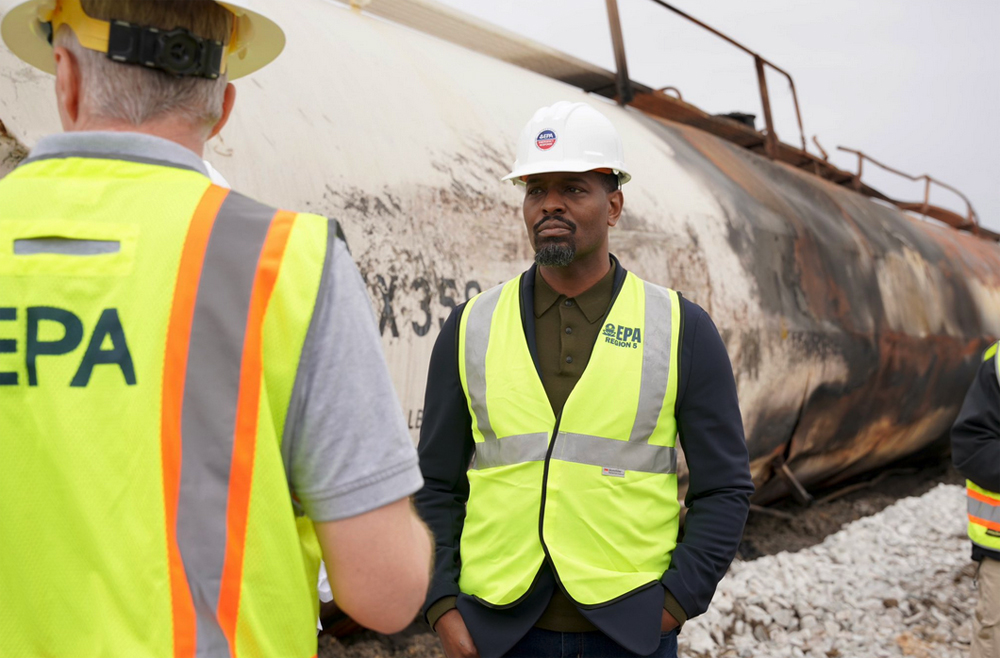 Men in high-visibility vests in front of fire-damaged tank car