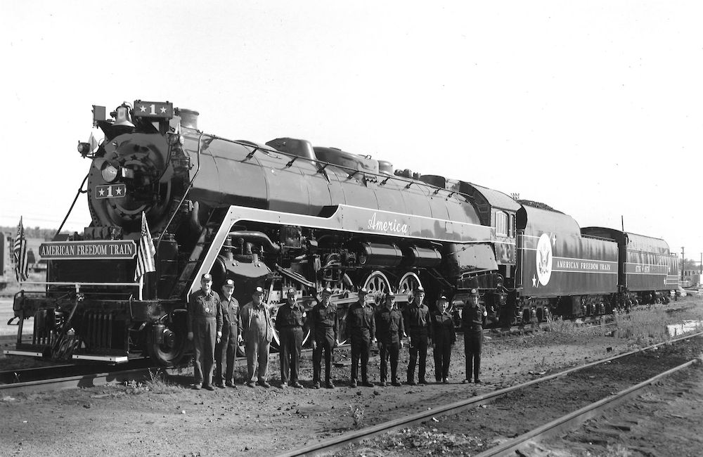 Steam locomotive on display with crew posing for a group photo.