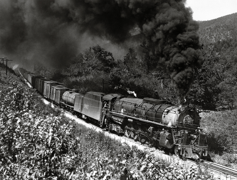 A steam locomotive with thick smoke hauls a freight train.
