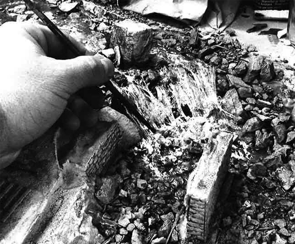 Malcolm Furlow's waterfall modeling technique: black and white photo showing hand with paintbrush applying white paint to a model waterfall