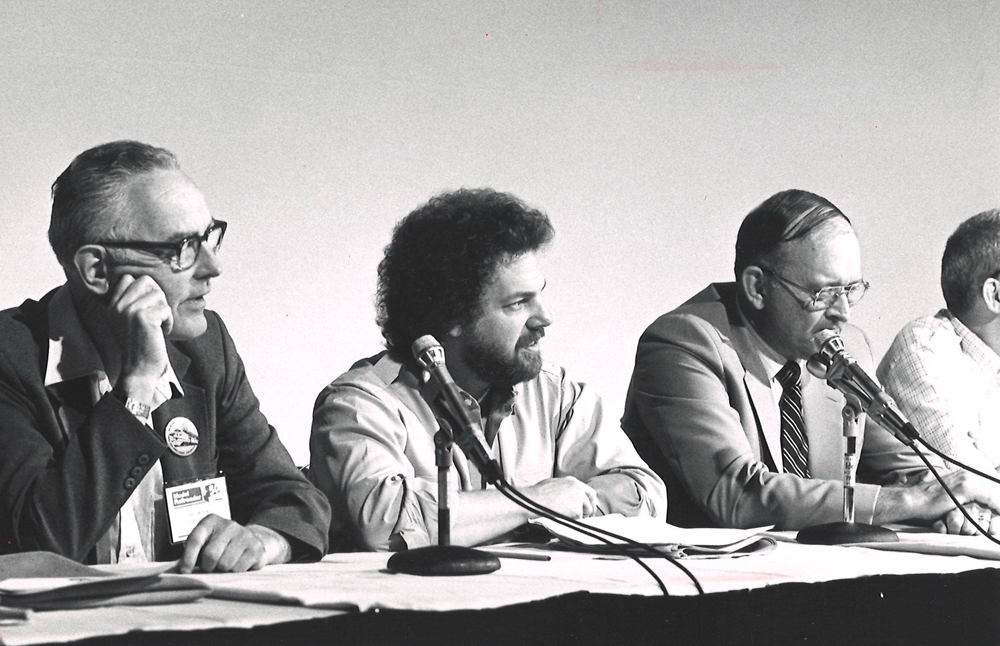Black-and-white photo of three men at panel discussion.
