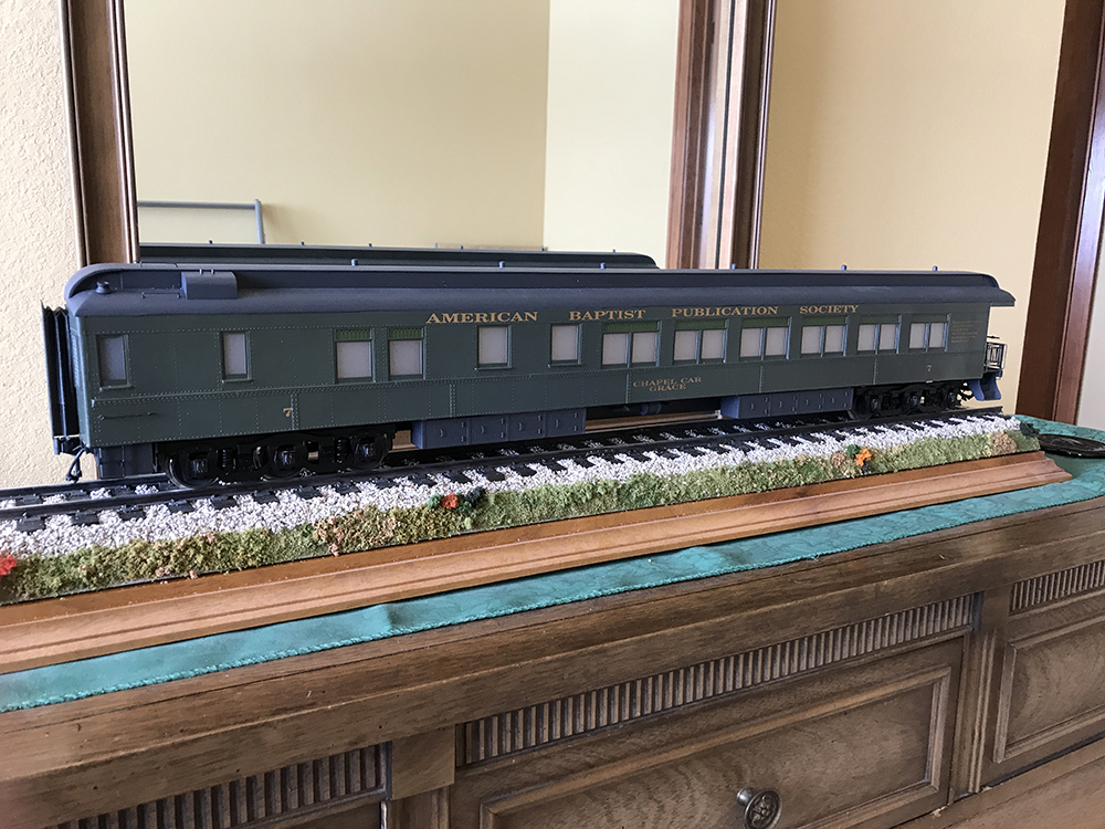 Large, dark green model passenger car on wood presentation base with model track