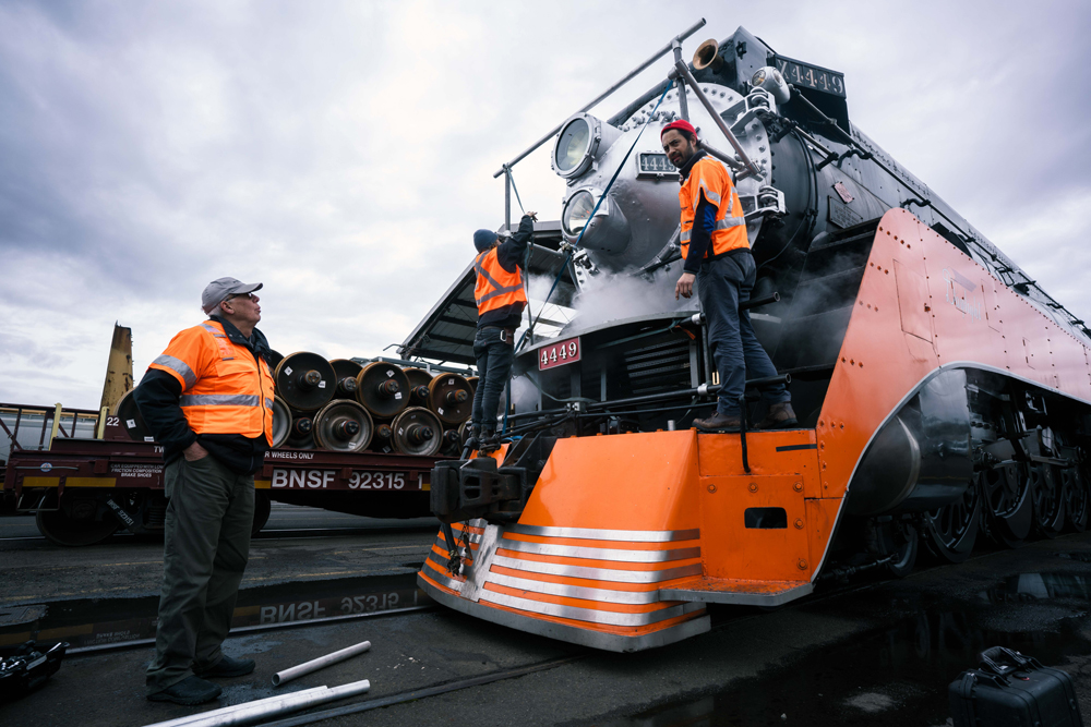 three men in orange safety vests by train