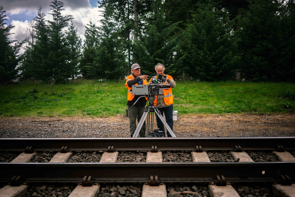 two men in vest trackside with Imax camera