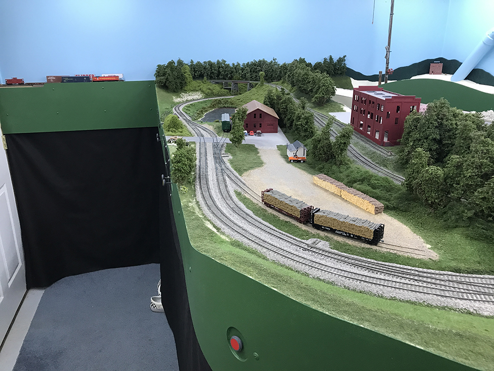 Carolina Sandhills Lines layout: Model train set up with green hills and trees, blue sky, and black curtains hiding the train table’s legs