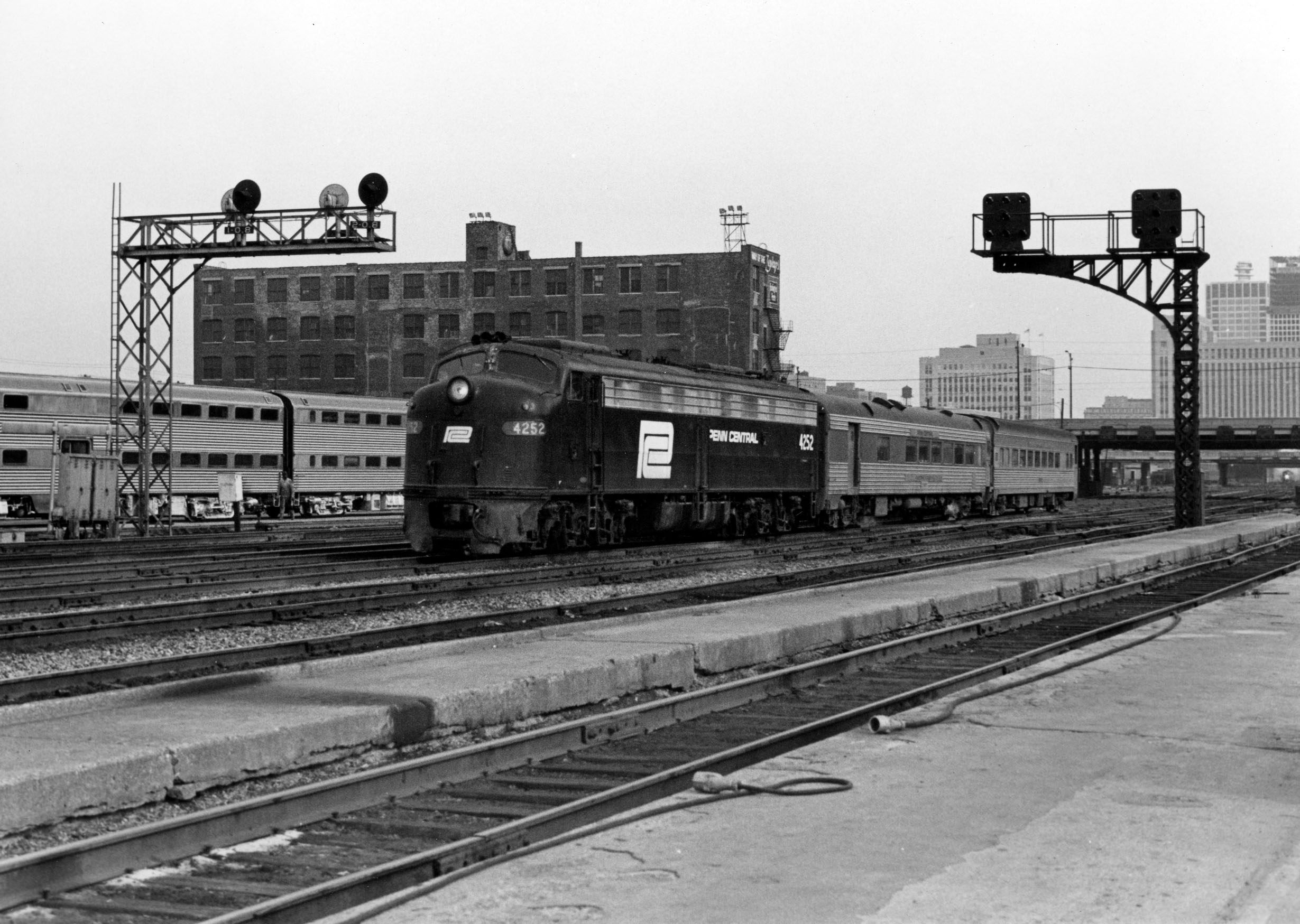 Black-and-white diesel locomotive with two passenger cars under elevated signals