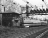 Streamlined Penn Central passenger train passes brick interlocking tower under wire