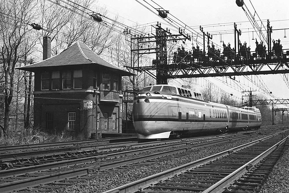Streamlined Penn Central passenger train passes brick interlocking tower under wire