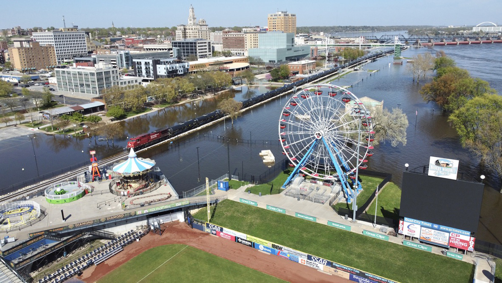 Train on track surrounded by floodwaters with baseball stadium in foreground