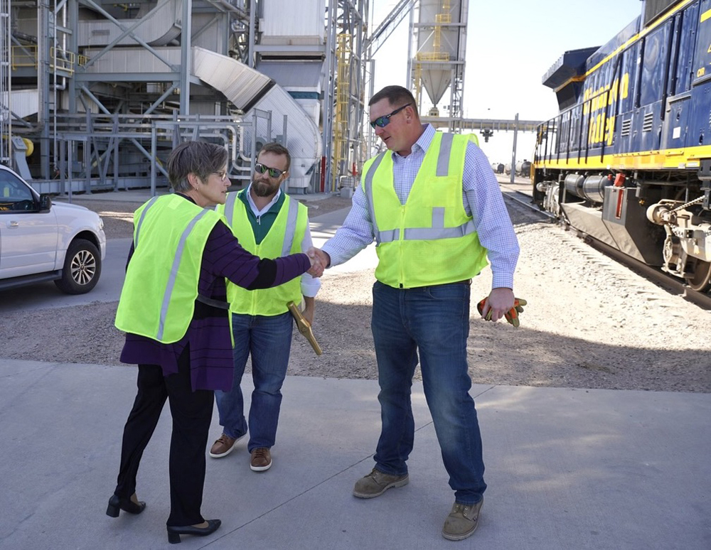 Woman and two men in high-visibility safety vests with locomotive in background