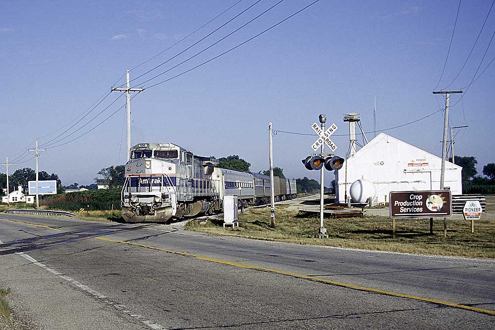 Silver-and-blue diesel locomotive with passenger train at road crossing