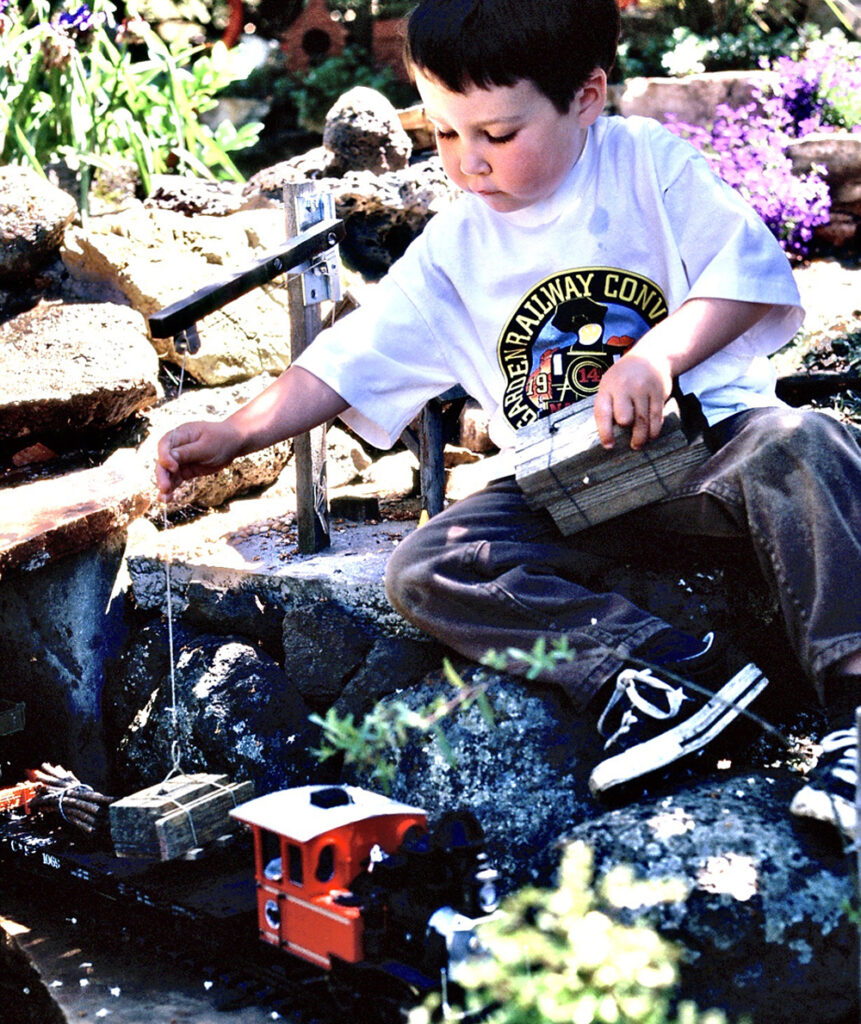 young boy sitting near garden railway