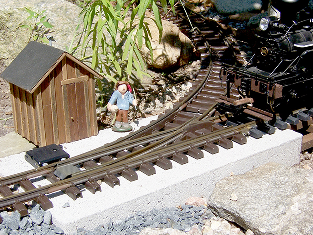 black locomotive approaches turnout with figure and small building