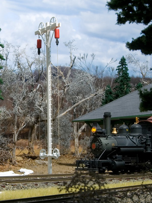 A small black steam locomotive passes a white trackside mast holding two red markers aloft on pulleys