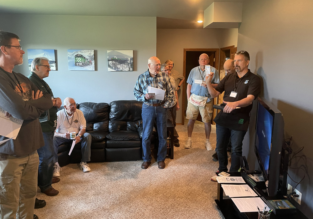 A man in a black shirt addresses several others in a basement rec room