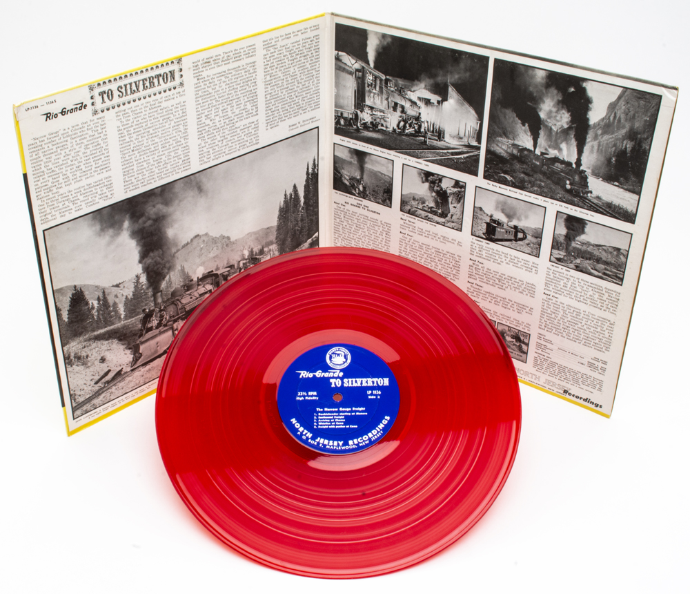 Photo of translucent red record in front of gatefold LP cover.