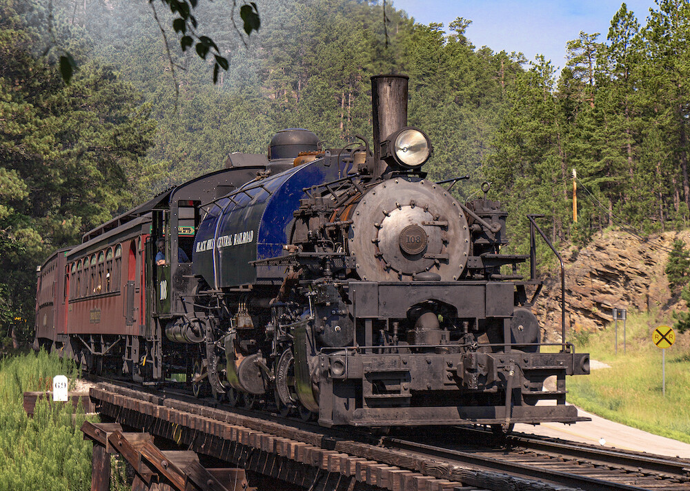 Mallet-type steam locomotive pulls excursion train through the woods