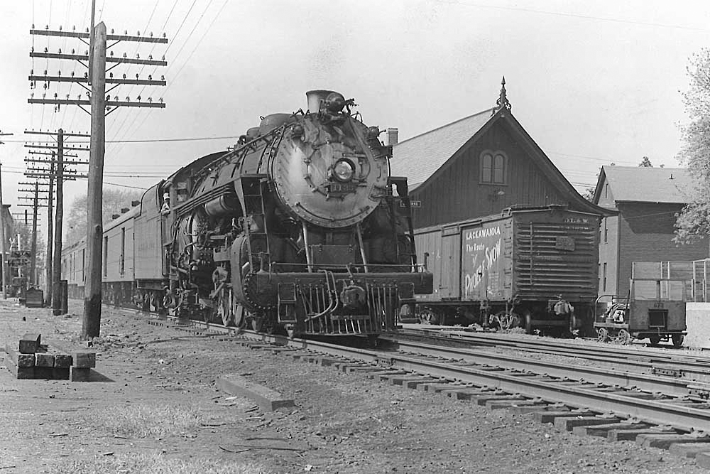 Steam locomotive with passenger train passes boxcar by station