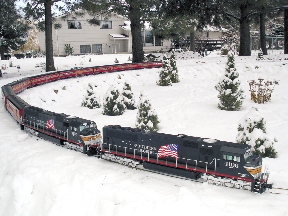 black model diesel with long train on curve and a snowy scene on garden railway