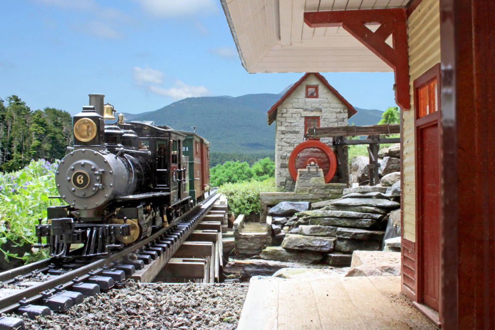 model steam locomotive approaches station on garden railway with blue sky in background