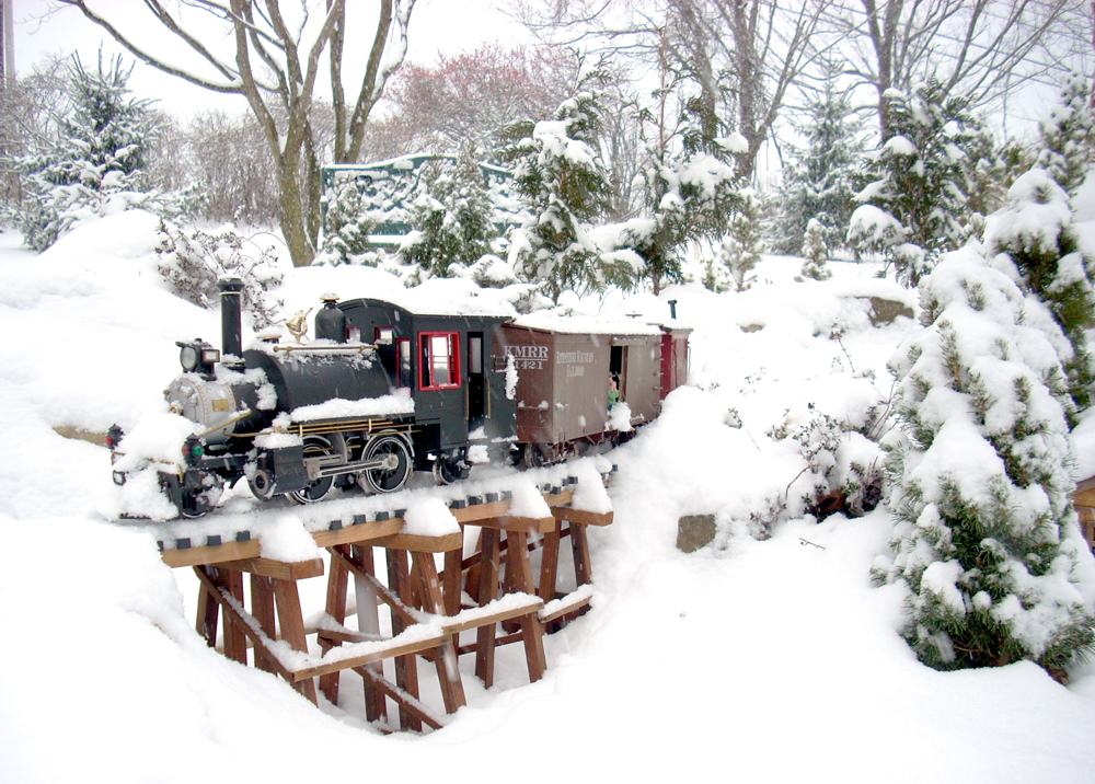 snowy scene with steam locomotive crossing bridge on garden railway