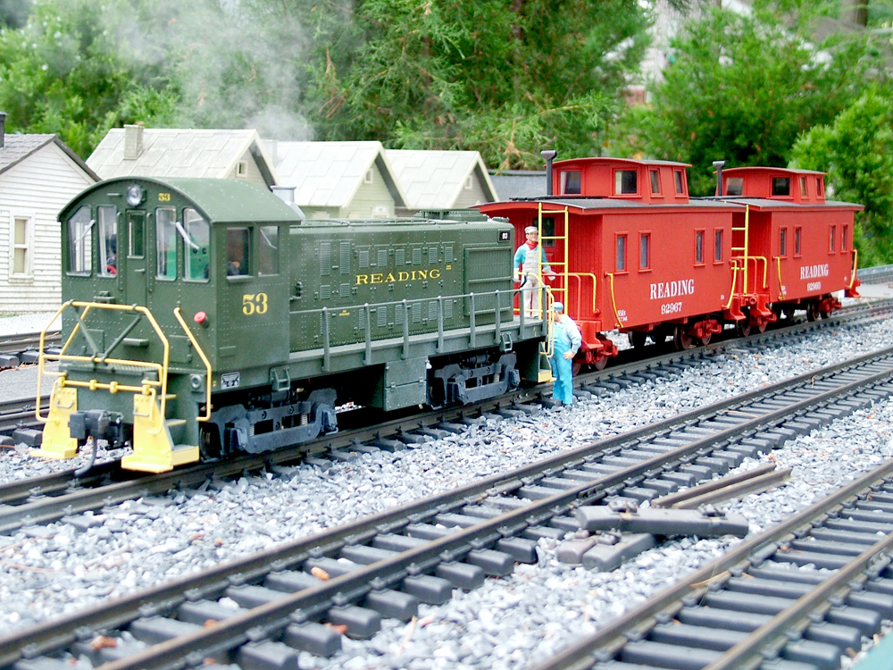 two red cabooses being pushed by a green switcher