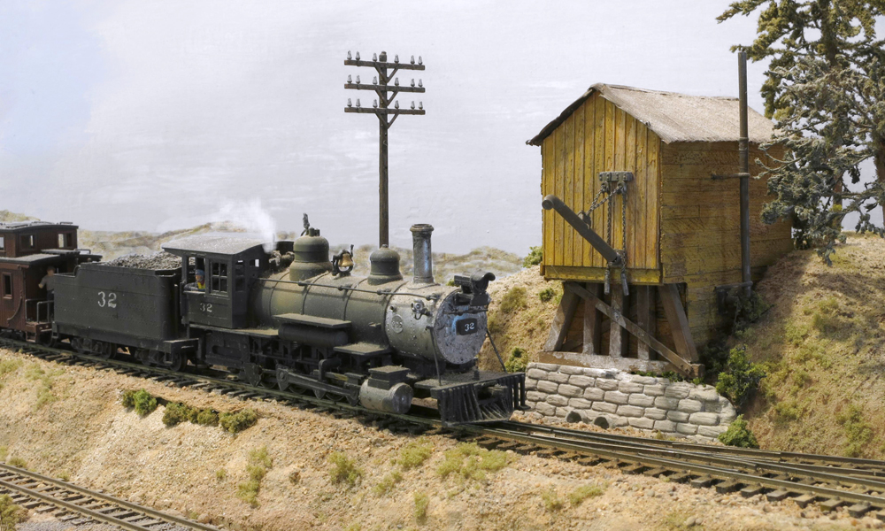 A steam engine trailed by a caboose pulls to a stop at a square wooden water tank