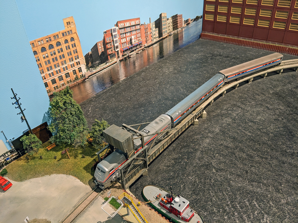 Model passenger train crosses over river.