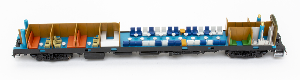 Model train passenger car with shell removed, revealing small blue and gray chairs and light blue flooring.