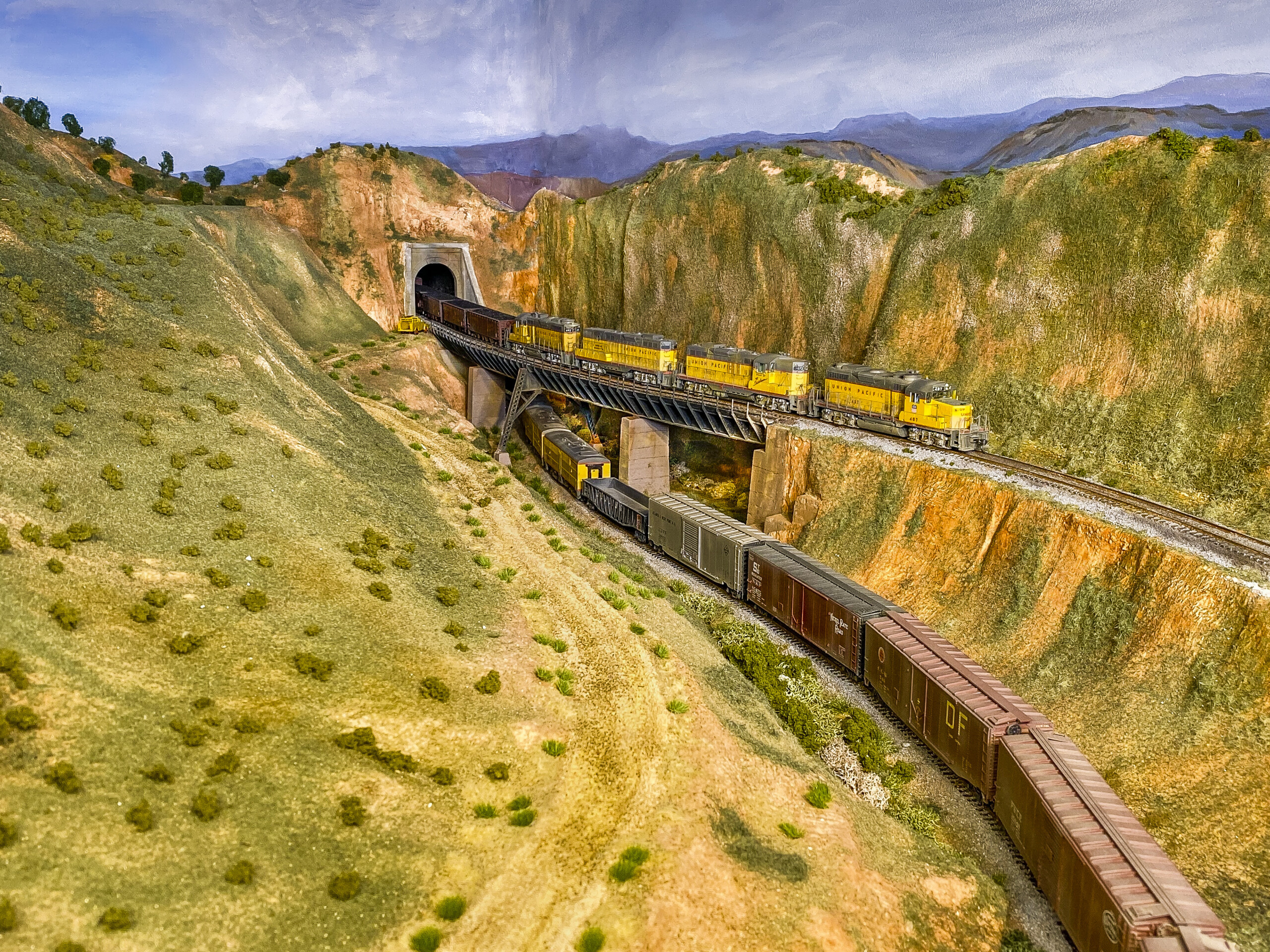 Two trains are shown entering and exiting from tunnels, with one crossing over a bridge and one passing under it.