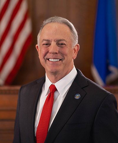 Man in suit with U.S. and state flags in background