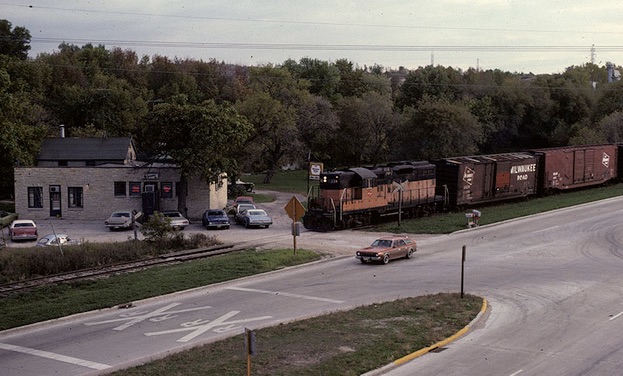Orange diesel locomotive with freight train by stone building