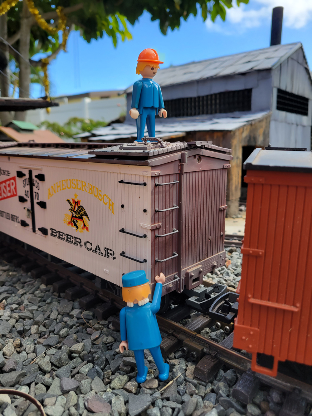 Two figures next to a model refrigerator car on a garden railway