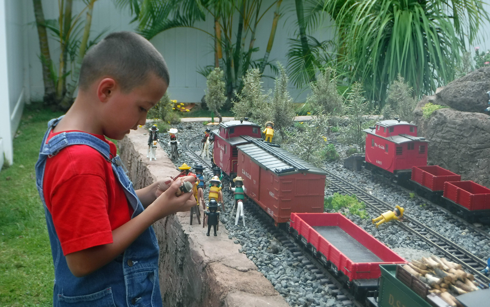 child plays with figures next to garden railway