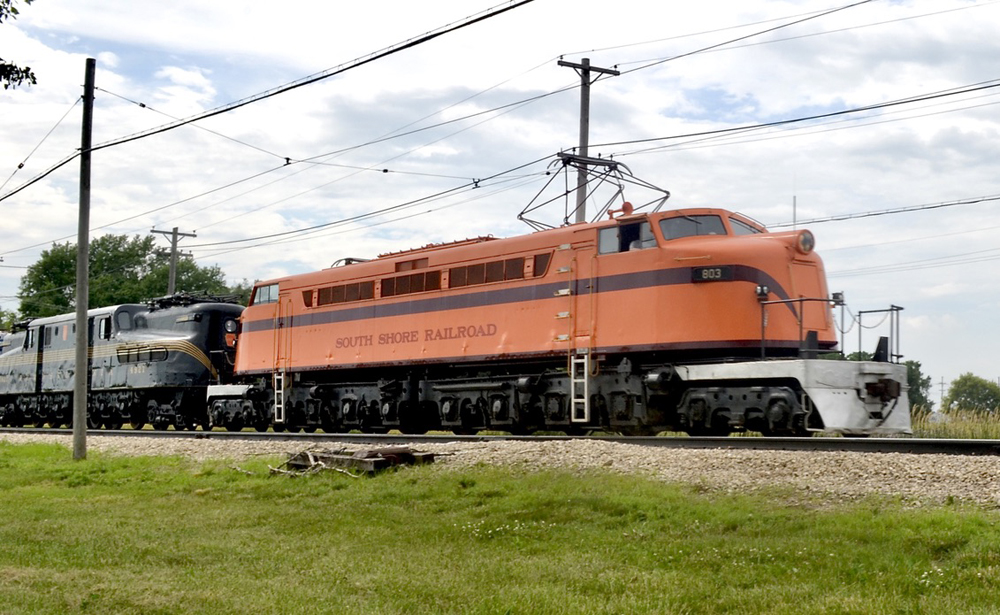 Orange electric locomotive pulling green electric locomotive