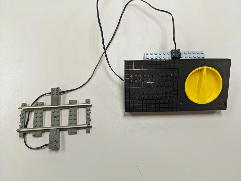 Gray LEGO train track with silver rails on top and black and yellow transformer
