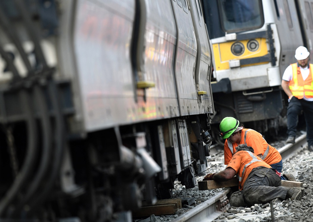 Worker look under derailed commuter car