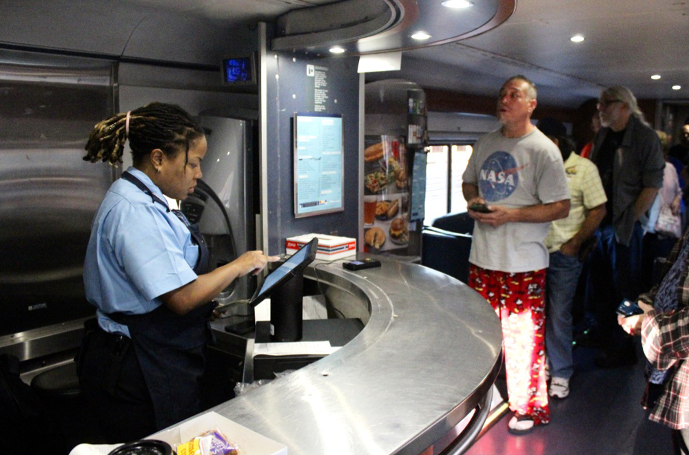 Woman working behind counter in cafe car with people waiting in line