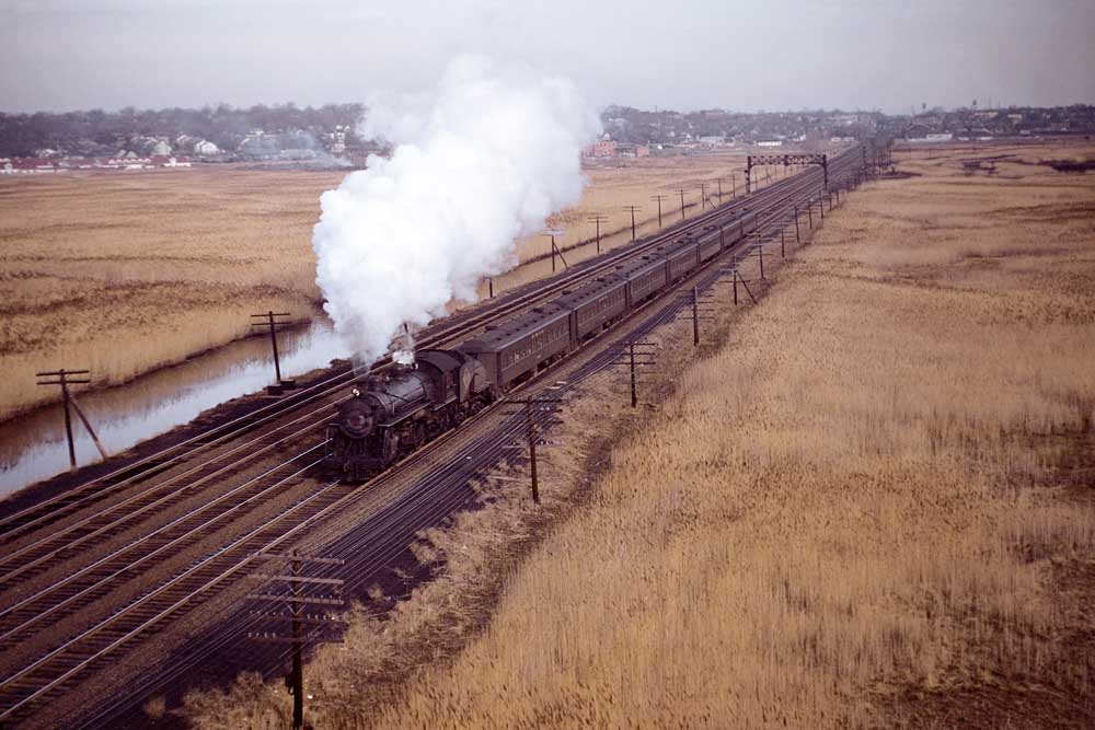 Smoking steam locomotive with passenger train in open meadow of Erie Railroad history