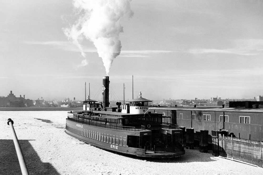 Smoking steam ferry boat in ice-covered water by pier of Erie Railroad history