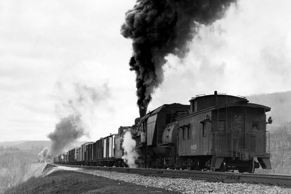 Caboose behind smoking steam locomotive shoving freight train of Erie Railroad history