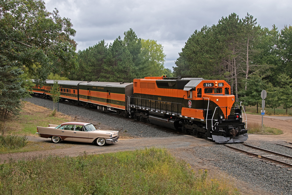 orange locomotive with 1950s car by it