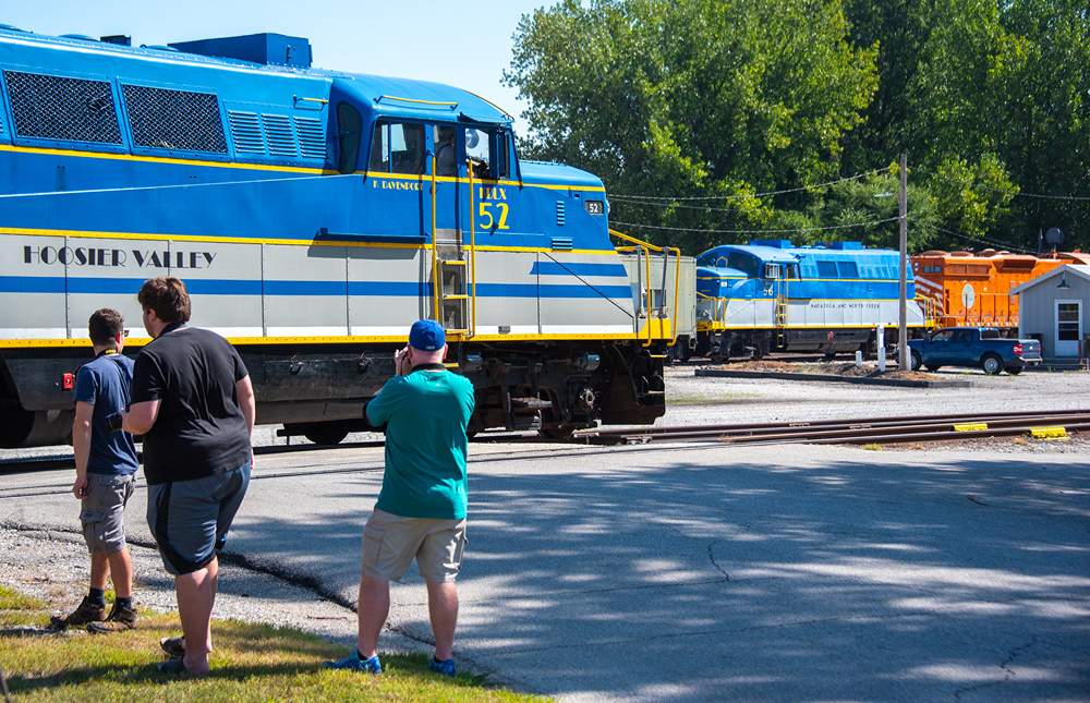 man photographing side of blue, yellow, and gray locomotive
