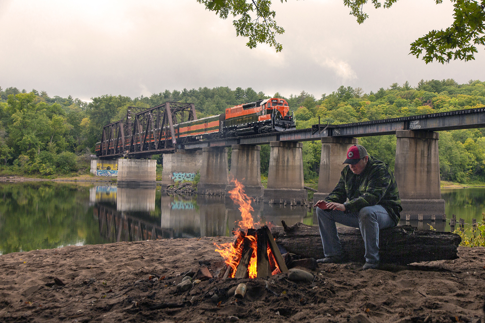 fire in foreground with train on bridge in back